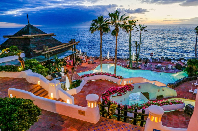 resort at sunset with palm trees, pool and sea view